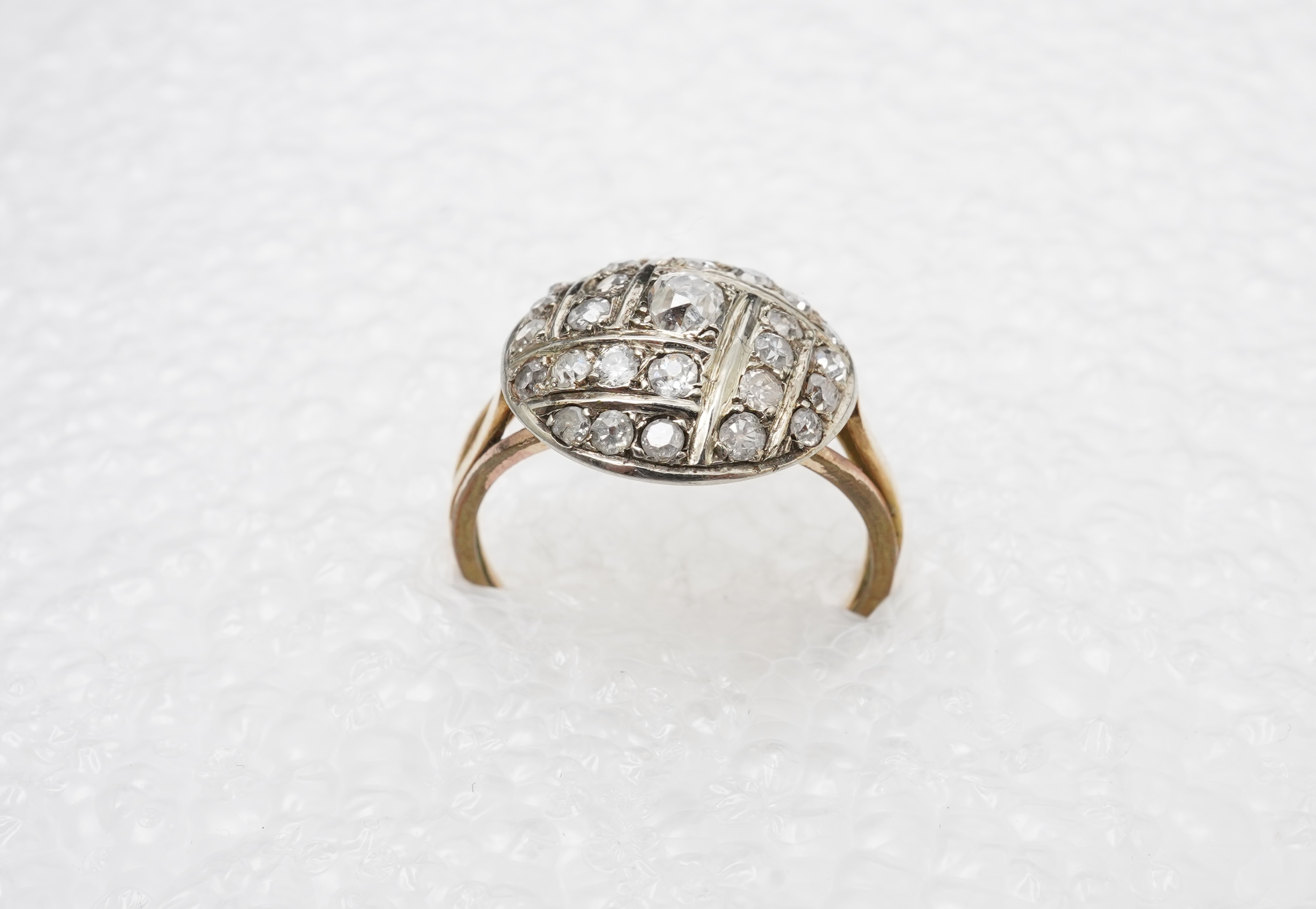 A diamond ring, centring on a circular motif of bombé design, set with geometric arrangements of cushion-shaped, single- and circular-cut diamonds totalling approximately 0.90 carats, to a gold band, size M1/2, indistinc
